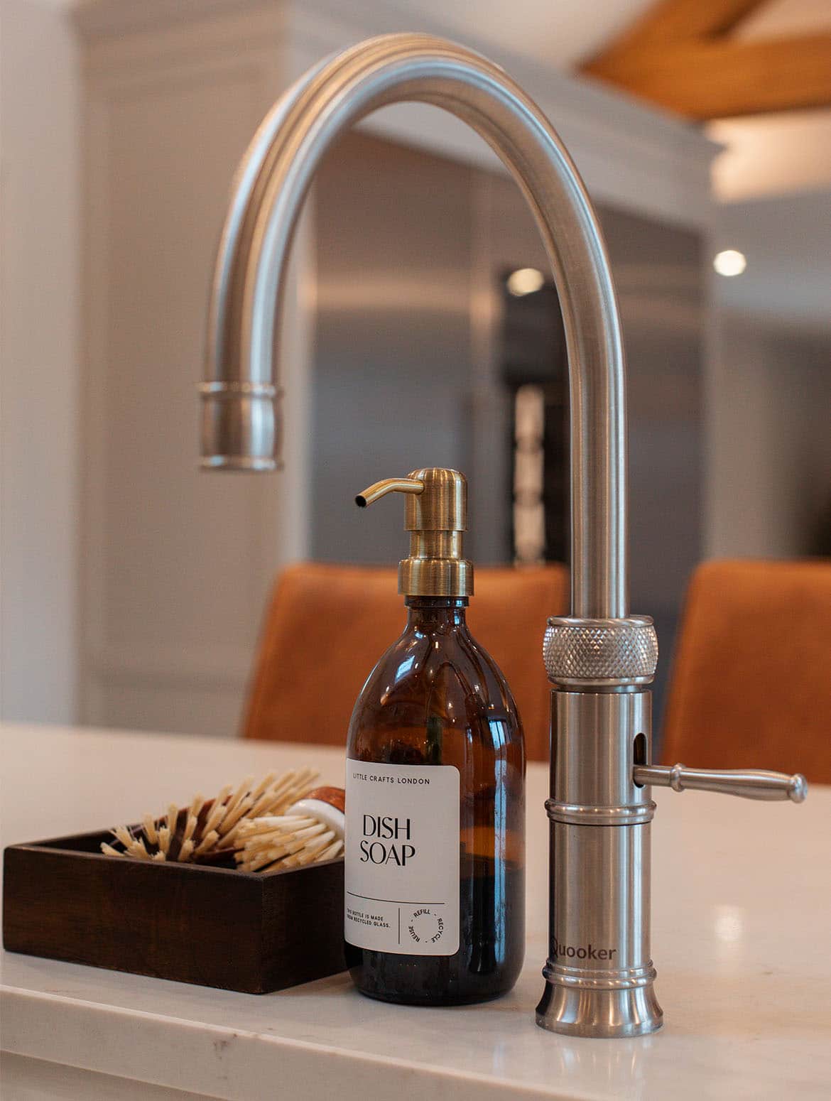 A traditional shaker kitchen in French Grey. A stainless steel Quooker tap on a white island stands next to a dish soap dispenser and the brushes. 