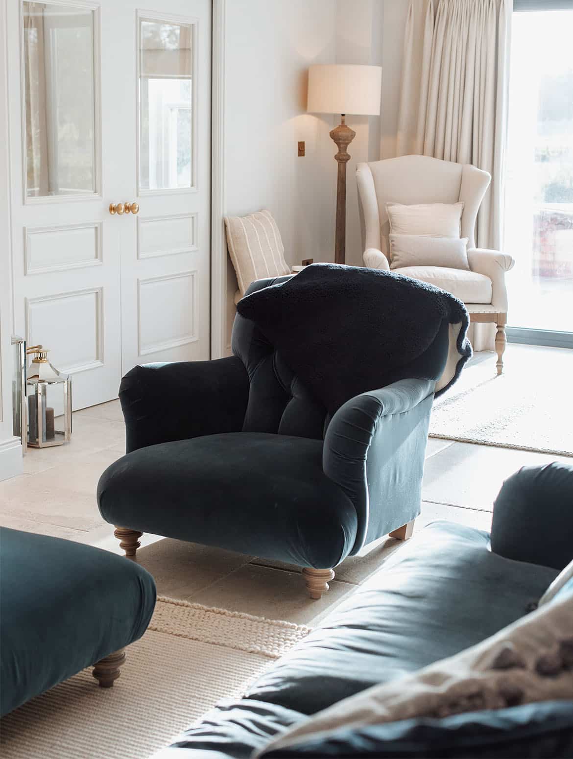 A media wall in French Grey. A teal velvet Tetrad armchair stands opposite of a Tetrad teal velvet sofa. This seating accompanies the Edwardian cabinetry of the media wall off the open-plan traditional shaker kitchen. 