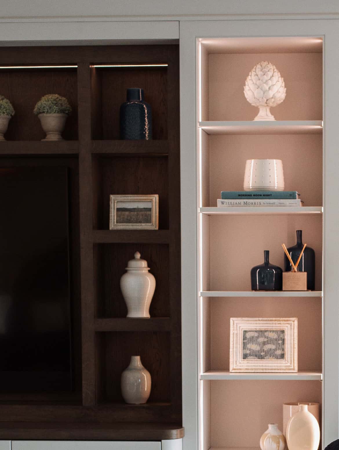 A media wall in French Grey. Bespoke Edwardian-style cabinetry surrounds the mounted TV. The main wall has a selection of ceramic plant pots and jars on the shelves while the columns feature more elaborate jars, urns, and vases.  