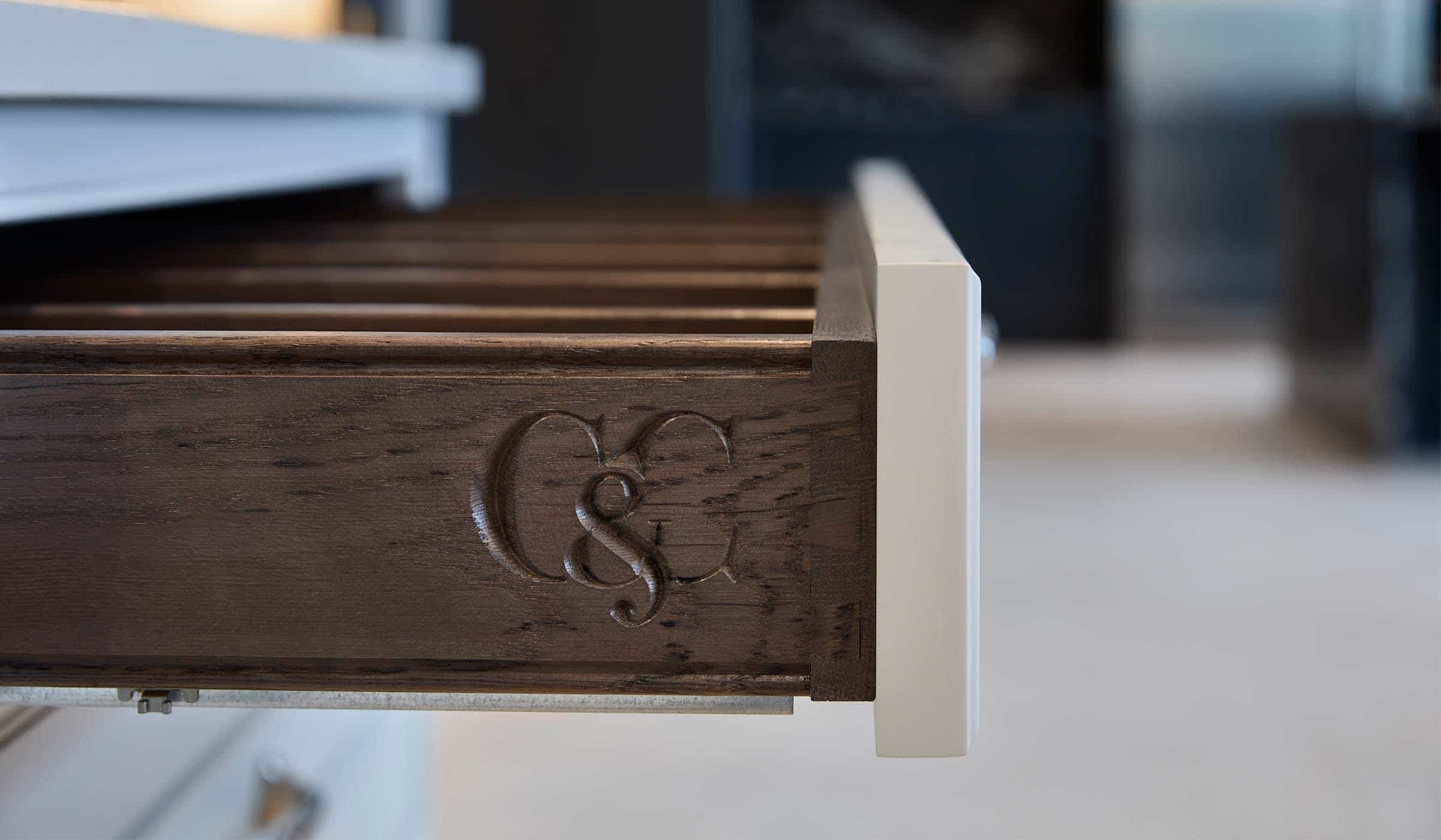 The Cook House Traditional Shaker Kitchen Project A traditional shaker kitchen in French Grey. An open drawer from the bespoke central island fitted with Snowy Ibiza quartz has the Cooks & Company logo engraved on along its edge.