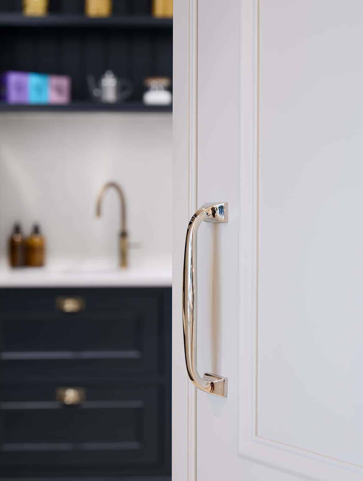 A traditional shaker kitchen in French Grey. The open door to the walk-in pantry has an Armac Martin handle with a satin lacquer. The cabinetry of the pantry can be seen beyond the open door. 