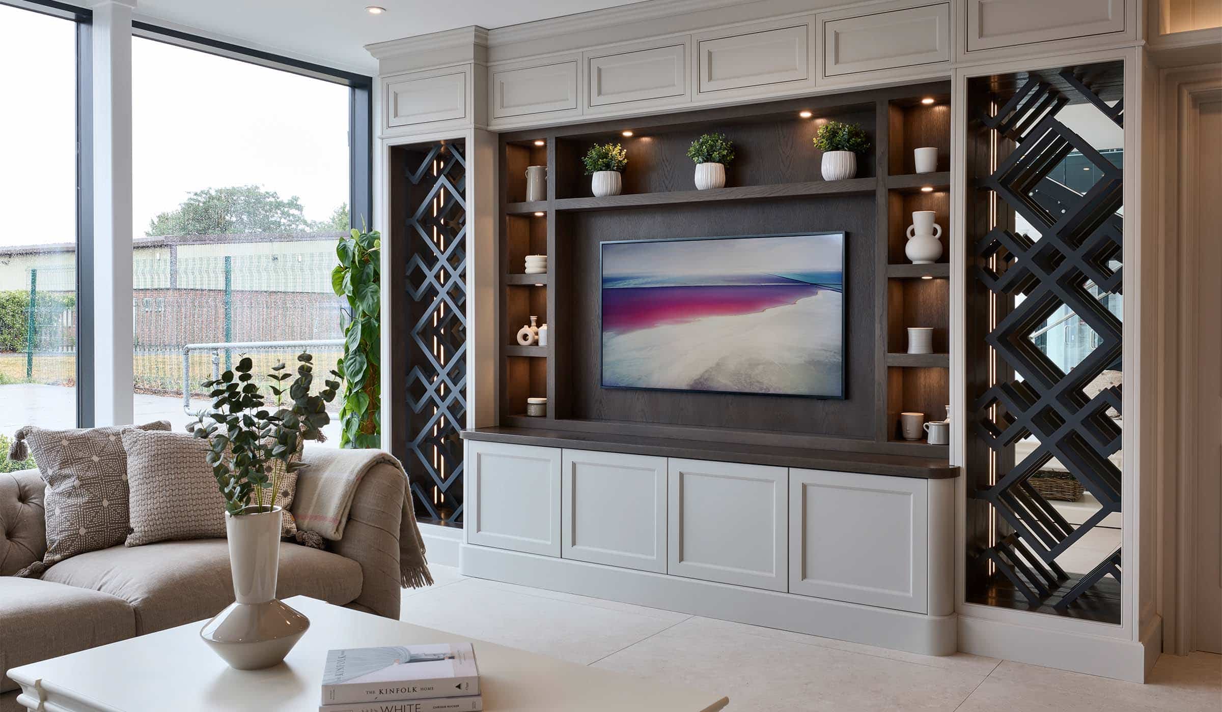 The Brunel Media Wall Project A bespoke media wall in French Grey. A bespoke media wall in French Grey. The mounted television, focal point of the wall, oversees a Tetrad sofa and a coffee table with a ceramic vase on its surface. Surrounding the television, bespoke shelving, set into floor-to-ceiling cabinetry, adds charm through its assortment of ceramic urns and vases, complementing the diagonal woodwork of the main pillars to the cabinet.