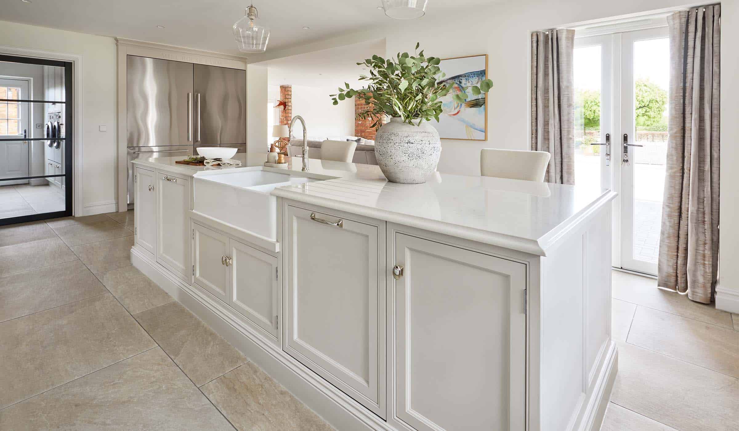 The Fox Traditional Shaker Kitchen Project A traditional shaker kitchen in French Grey. The island fitted with Armac Martin handles and fitted with a Quooker tap, stands centrally in the kitchen. It has an American-style double fridge freezer from Fisher and Paykel to its rear and the utility room is just visible beyond as well.