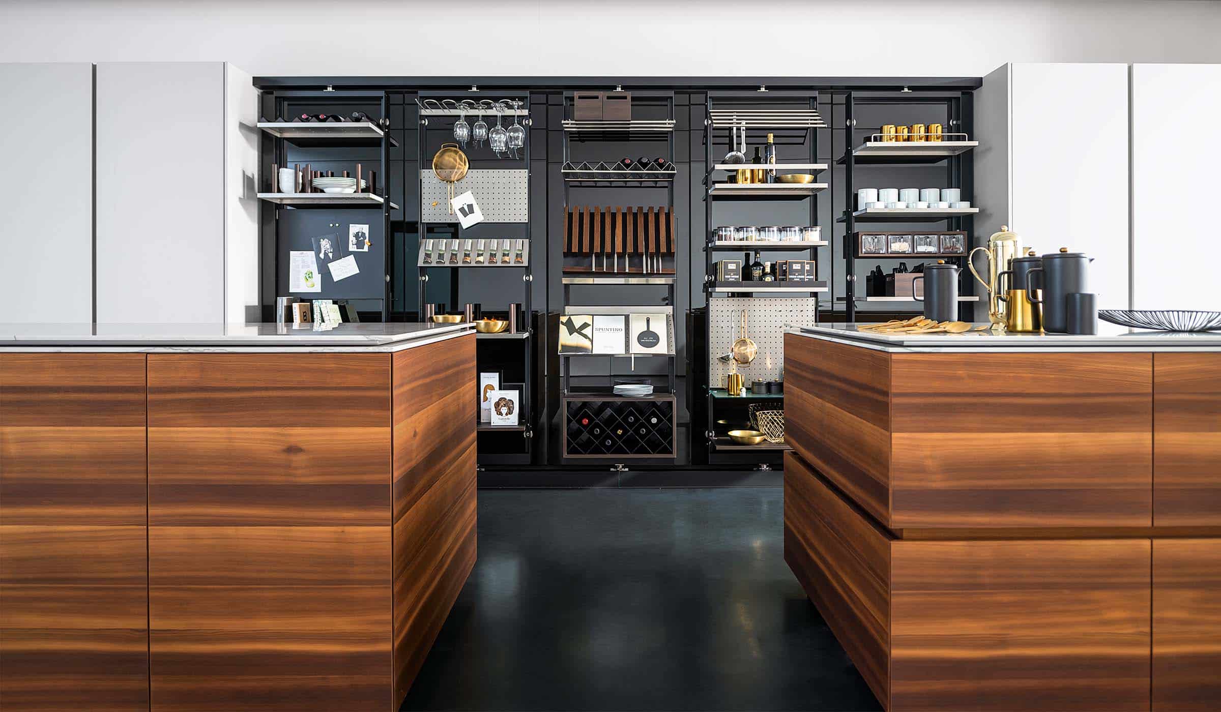 The Larch Modern Kitchen Project A modern kitchen with quartz-top islands. A modern kitchen with quartz-top islands. The dual central kitchen islands stand proud to the sleek cabinetry against the far wall which encloses built-in ovens on one side and culinary items in the middle. The open door reveals an ergonomic selection of shelves and racks that have items ranging from wine glasses to a sieve and dishes.