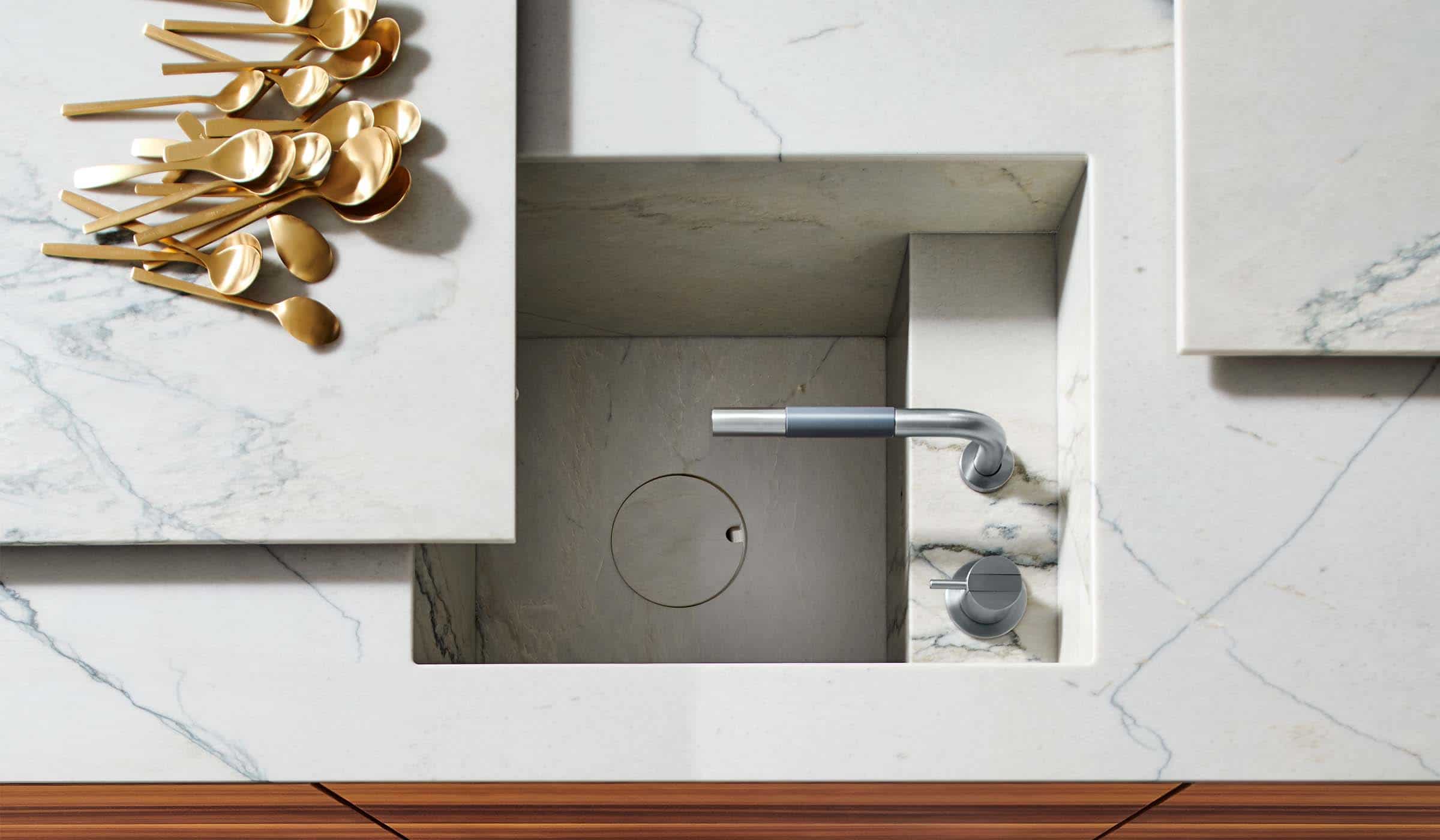 The Larch Modern Kitchen Project A modern kitchen with quartz-top islands. A close in of the sink and the two freestanding chopping and draining boards—cutout squares of the same quartz material—that overshadow the sink cut into the quartz itself. A selection of gold spoons line the left quartz cutout.