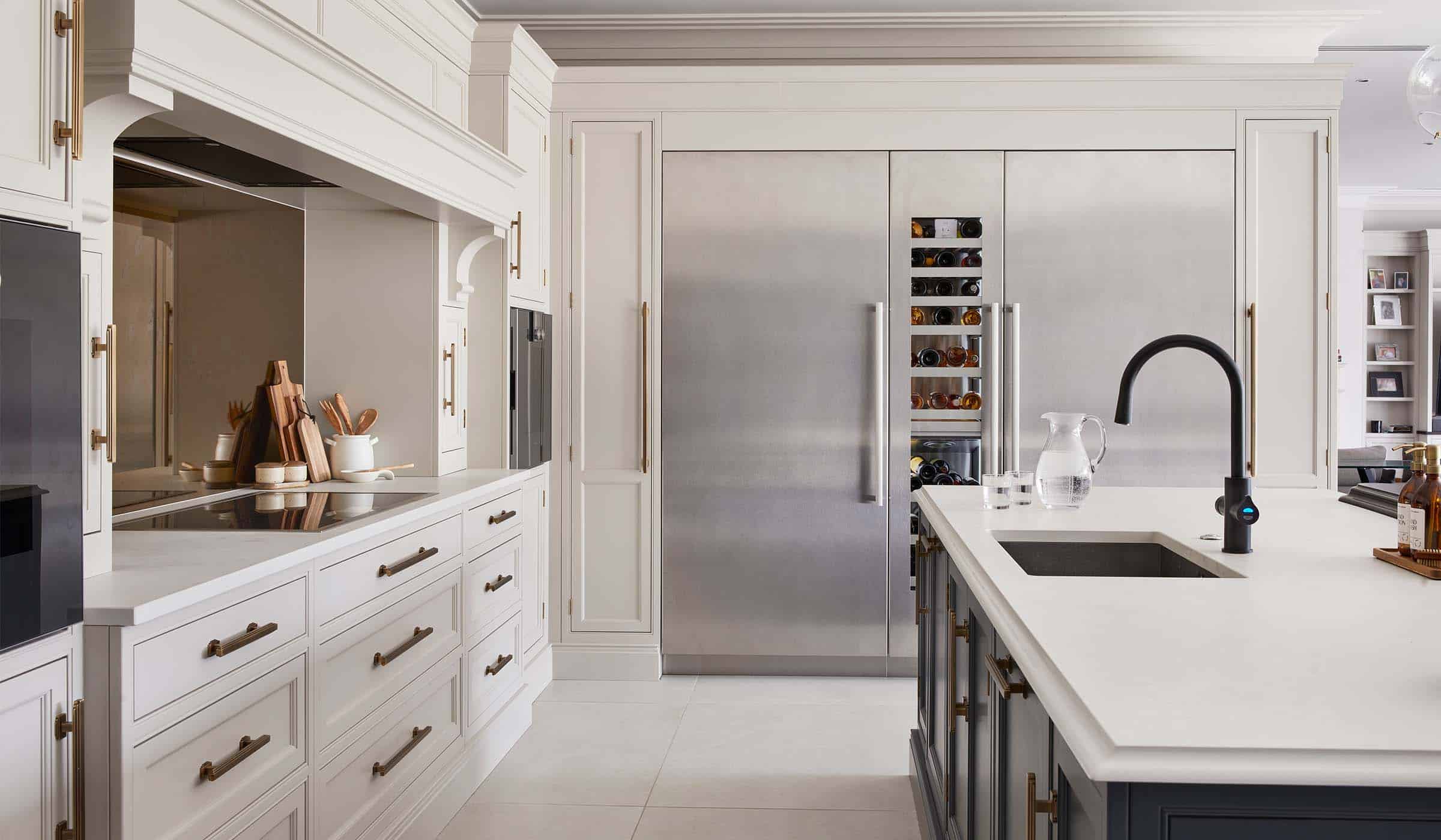 The Tawny Traditional Shaker Kitchen Project A traditional shaker kitchen project in off-black. A central island with bespoke cabinetry and a white worktop has a black Zip tap set into it. A jug of water with two glasses stands on the edge, while beyond the island bespoke cabinetry surrounds a Liebherr Monolith fridge and freezer. In between the two there’s a central wine cabinet as well. The French Grey cabinetry and above and the mount opposite the island offset the off-black.