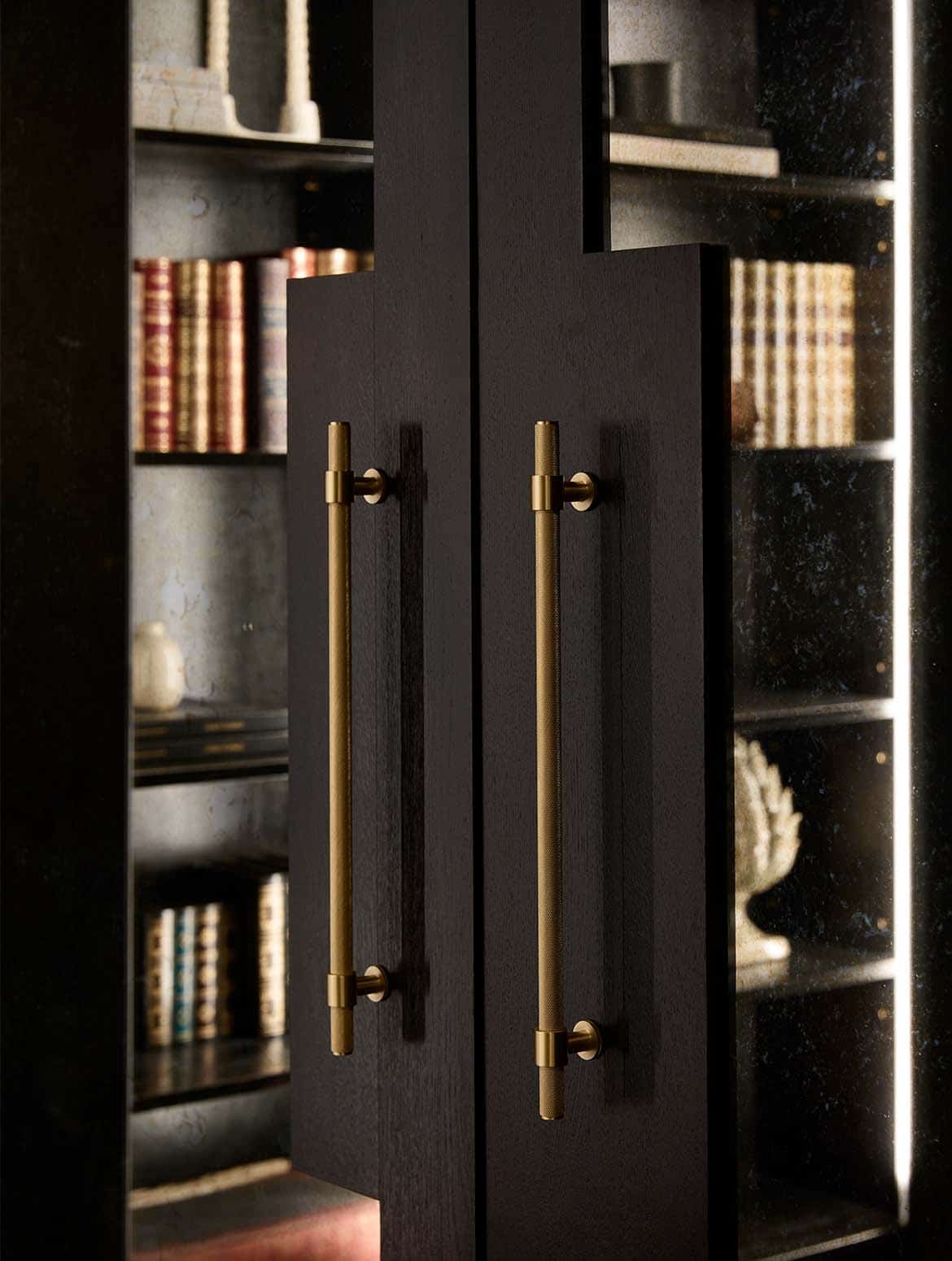 A bespoke bar area in onyx. The off-black panelling of the doors with inlaid mirrors reflect the library shelves ahead of them. 