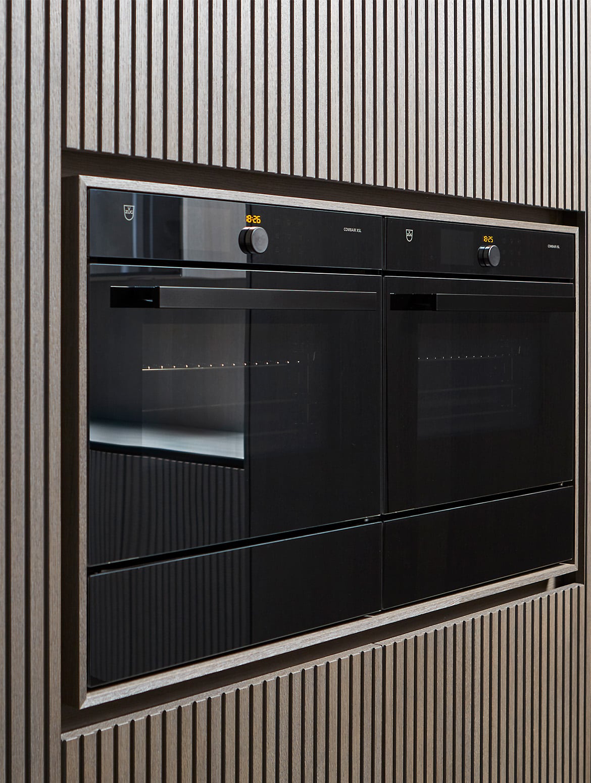 A modern kitchen in smoked wood finish. The bespoke cabinetry with a smoked wood finish surrounds premium V-Zug ovens.    