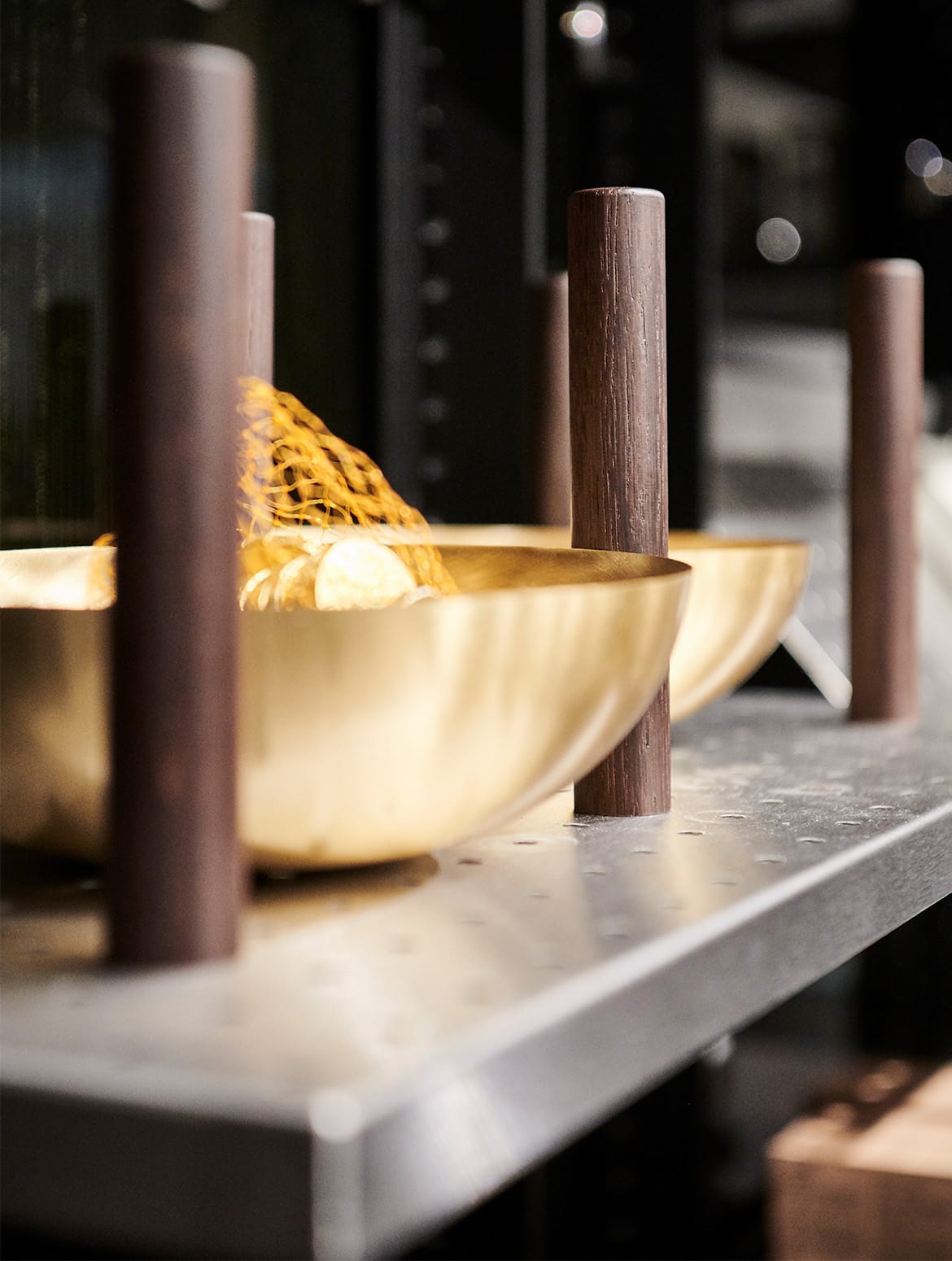 A modern kitchen with quartz-top islands. A close in on one of the shelves within the middle cabinet shows two gold bowls with a sack of gold chocolate coins in it. The perforated metal shelf uses wooden dowels at equal spaces to ensure the bowls remain separate.  
