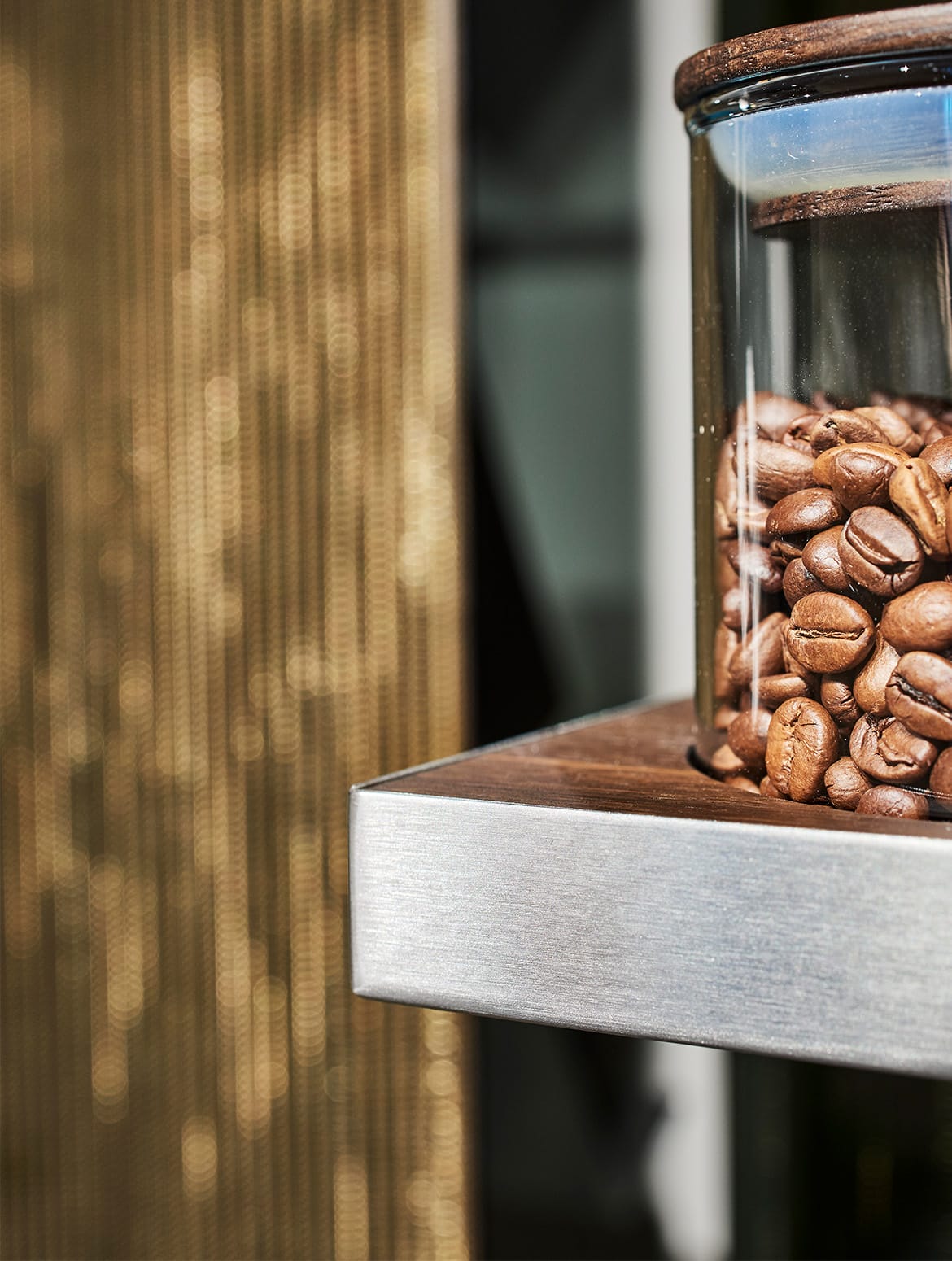 A modern kitchen with quartz-top islands. A close in on one of the shelves within the middle cabinet shows a glass jar of the coffee beans. 