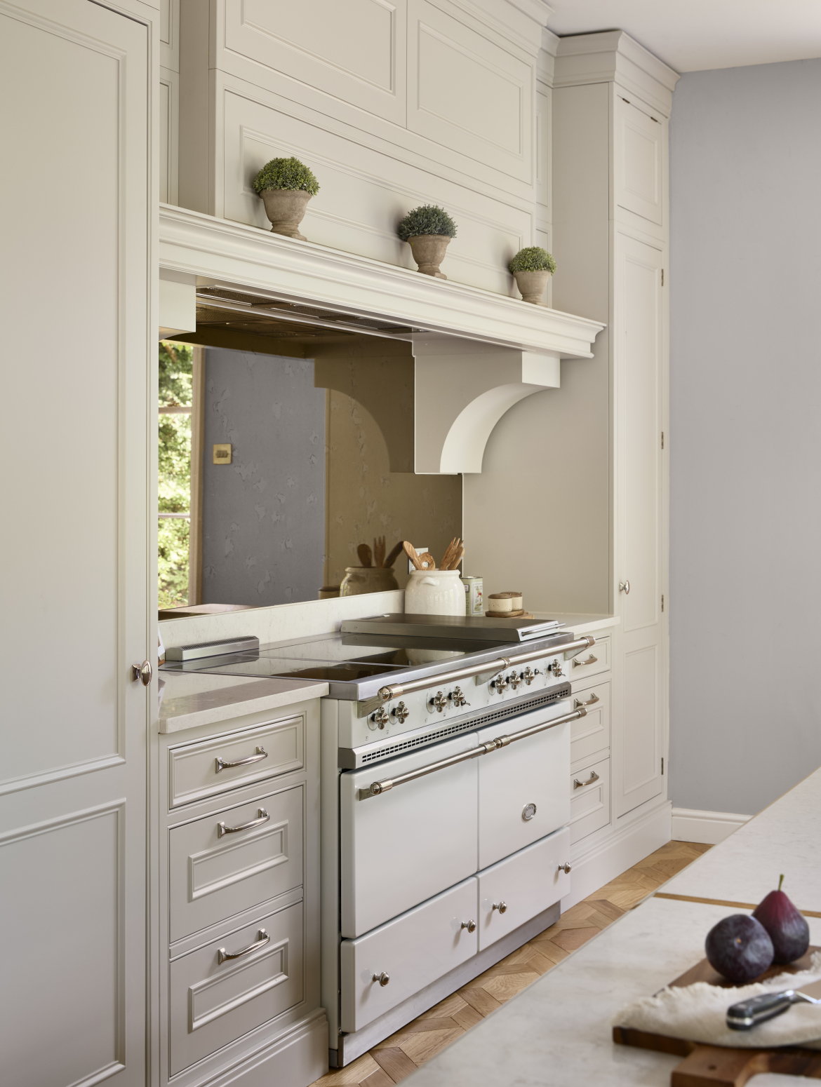 A traditional cream shaker kitchen with bespoke cabinetry around a white Lacanche range cooker. The range cooker stands proud to the tall cupboards either side and to the easily-accessible cupboards beside the cooker itself.