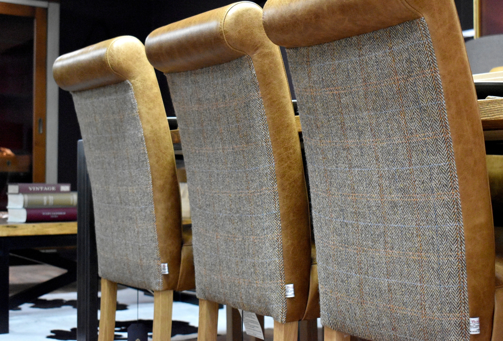 A close in view of three upholstered high chairs in tweed stood before a high table and ahead of a metal-legged coffee table with three books stacked on their side on it. 