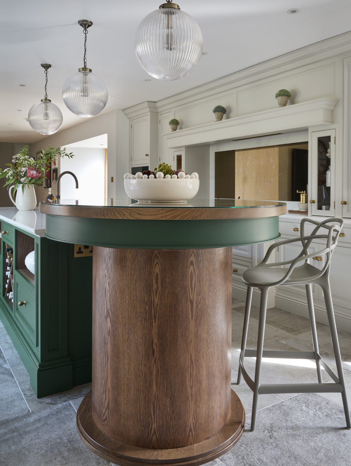 A traditional shaker kitchen with a two-tier island with green bespoke cabinetry. The second taller island has a band of Brunswick green to match the island behind. A metal high chair stands beside the second tier. 