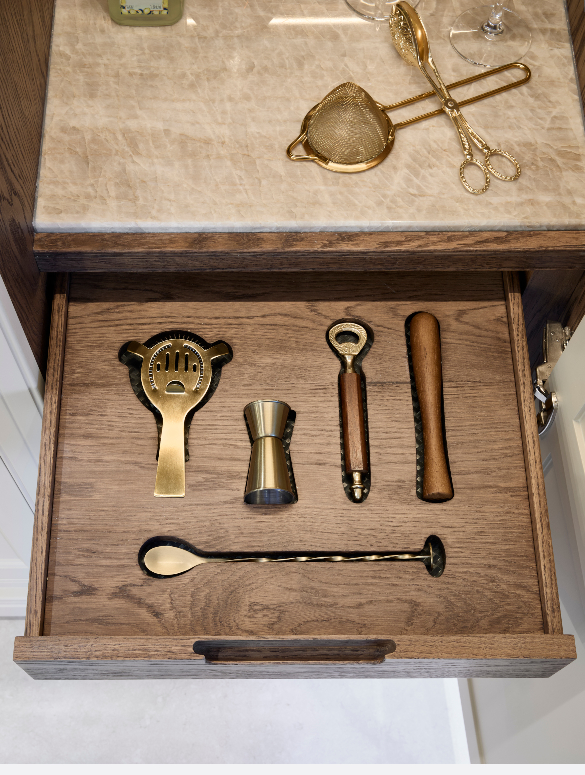 A traditional shaker kitchen in French Grey. The open drawer of the mixology section reveals all the required tools to make a cocktail. 