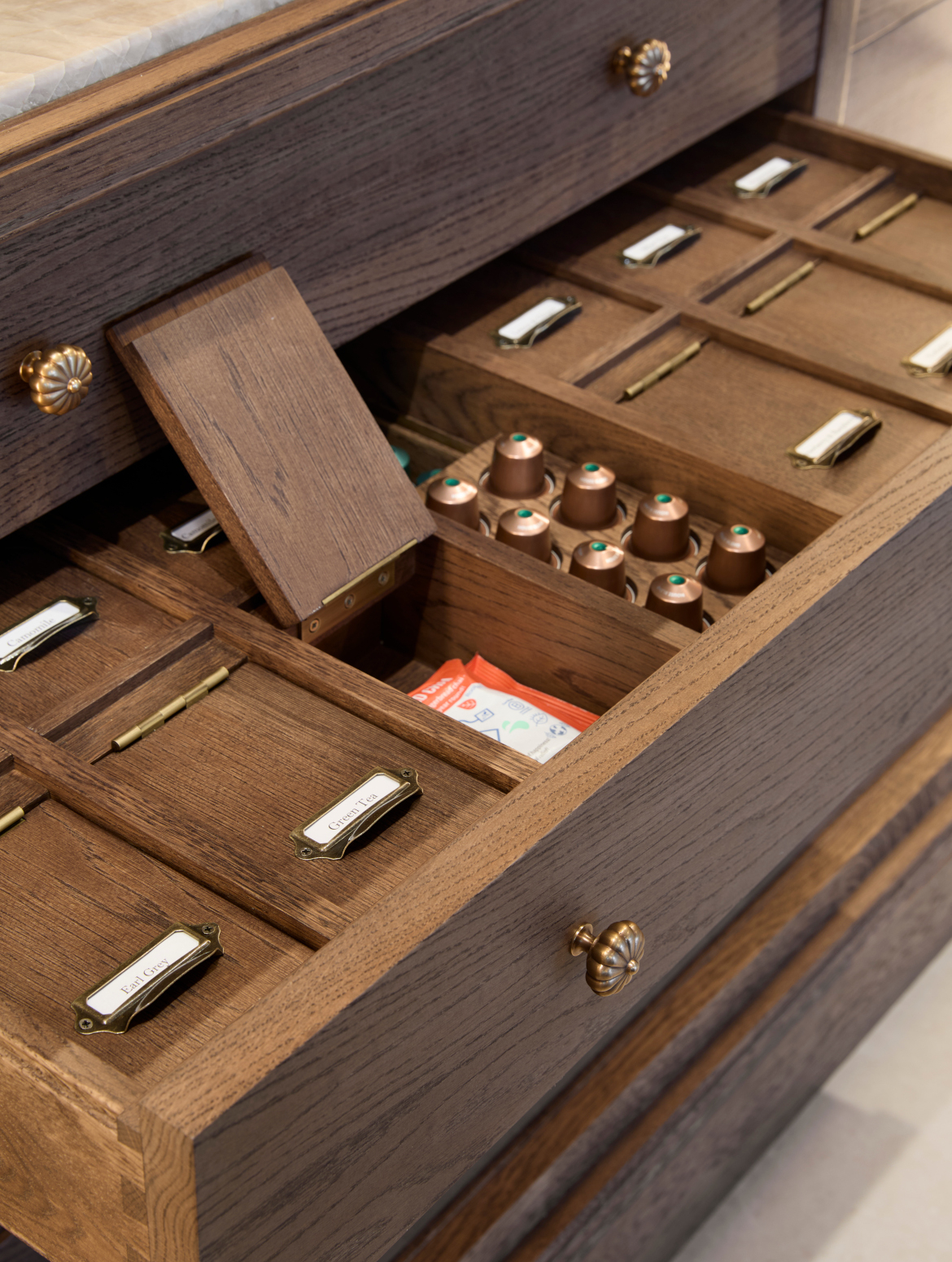 A traditional shaker kitchen in French Grey. An open pantry drawer with Armac Martin handles reveals separate section for different types of hot beverages. 