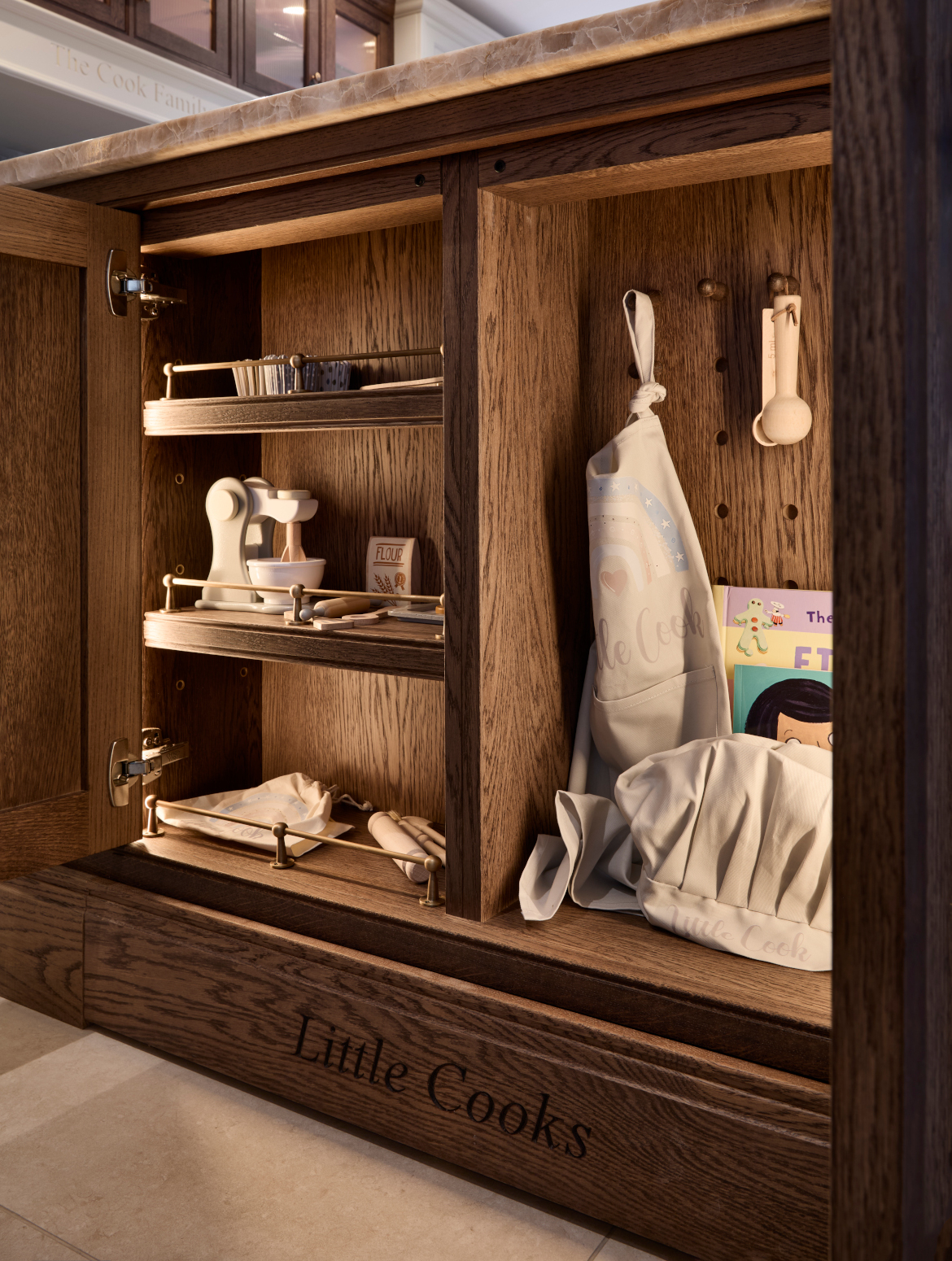 An image of a kitchen island with a cupboard fitted with children's utensils and baking attire.